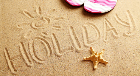 The word Holiday written in sand with flip flops and a star fish surrounding